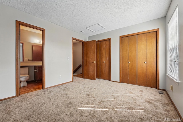 unfurnished bedroom with baseboards, carpet flooring, connected bathroom, visible vents, and multiple closets