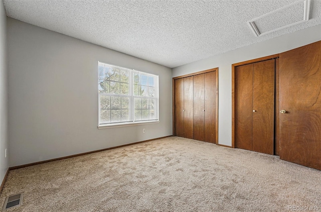 unfurnished bedroom featuring visible vents, multiple closets, carpet flooring, and a textured ceiling