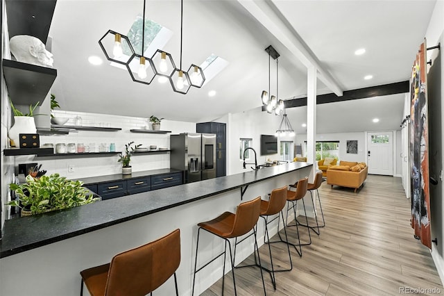 2500 Estes St, Lakewood, CO 80215 - kitchen featuring stainless steel fridge with ice dispenser, open shelves, a kitchen bar, dark countertops, and blue cabinetry