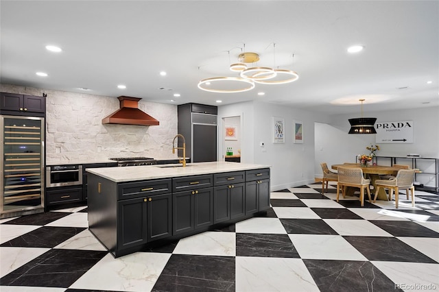 kitchen with an island with sink, hanging light fixtures, light countertops, premium range hood, and a sink