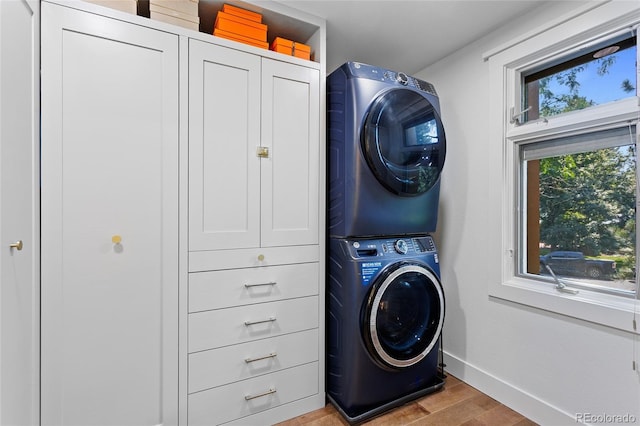 laundry area featuring stacked washer and dryer, light wood-style flooring, baseboards, and cabinet space