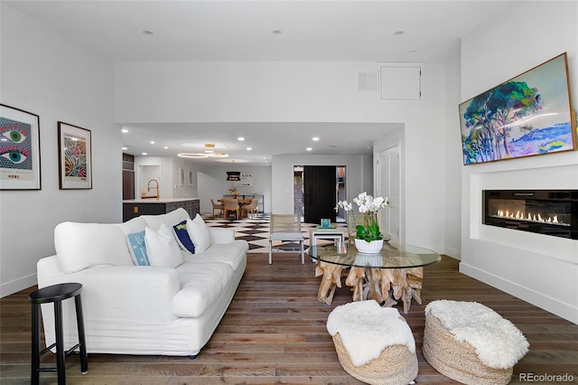 living area featuring a glass covered fireplace, recessed lighting, dark wood finished floors, and baseboards