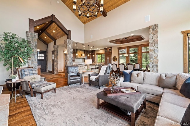 living room featuring wooden ceiling, high vaulted ceiling, a notable chandelier, dark hardwood / wood-style flooring, and decorative columns