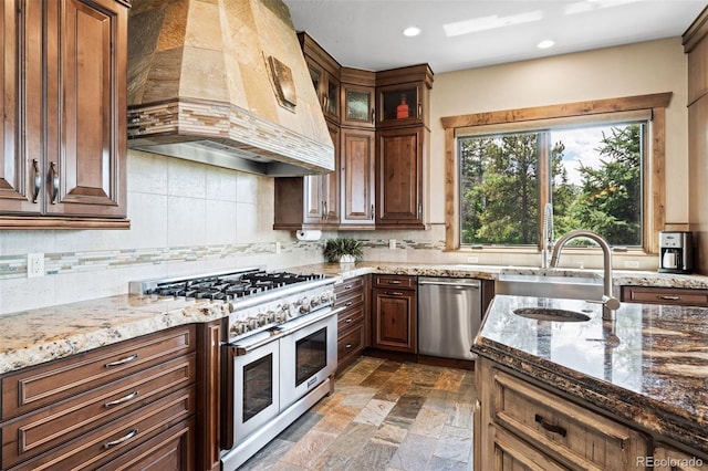 kitchen with backsplash, dark stone counters, custom range hood, stainless steel appliances, and sink