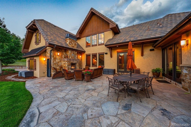 back house at dusk with an outdoor living space with a fireplace and a patio