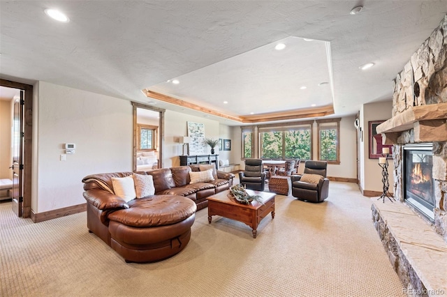 carpeted living room featuring a fireplace, a textured ceiling, and a tray ceiling