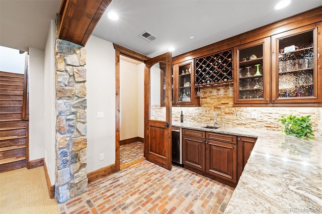 bar with tasteful backsplash, light stone countertops, and sink