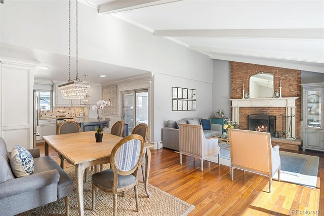 1100 Pontiac St, Denver, CO 80220 - dining space featuring a brick fireplace, light wood-style flooring, beamed ceiling, a chandelier, and crown molding
