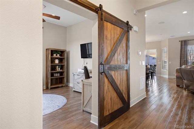 corridor with wood-type flooring, baseboards, visible vents, and a barn door