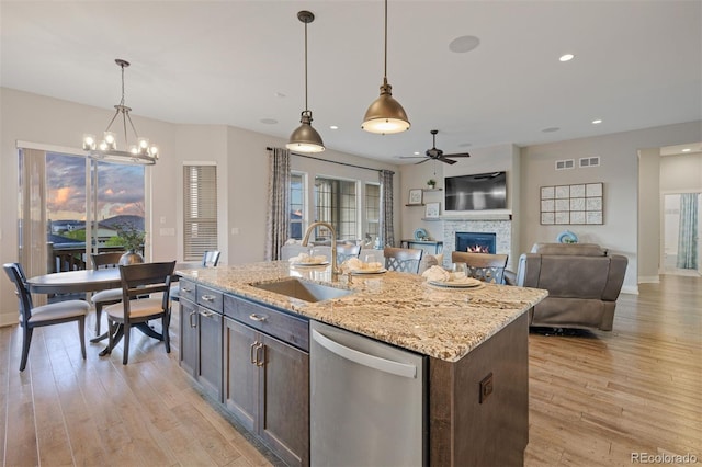 kitchen featuring stainless steel dishwasher, a sink, light wood finished floors, and a stone fireplace