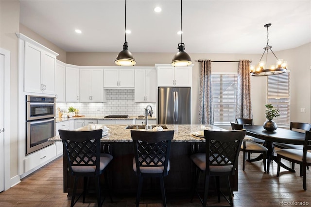 kitchen with appliances with stainless steel finishes, tasteful backsplash, dark wood finished floors, a sink, and a notable chandelier