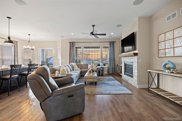 living room with visible vents, a glass covered fireplace, ceiling fan with notable chandelier, and wood finished floors