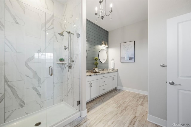 bathroom featuring vanity, wood finished floors, baseboards, a chandelier, and a marble finish shower