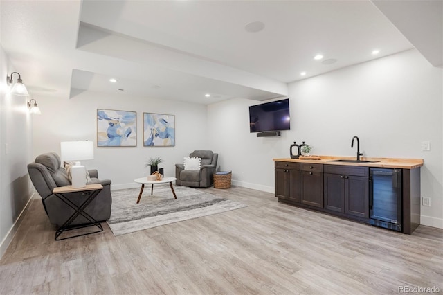 bar featuring a sink, light wood-style flooring, indoor wet bar, baseboards, and wine cooler