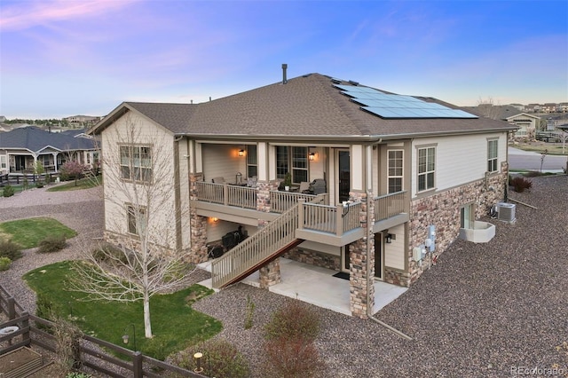 back of property with roof with shingles, stone siding, roof mounted solar panels, cooling unit, and a patio