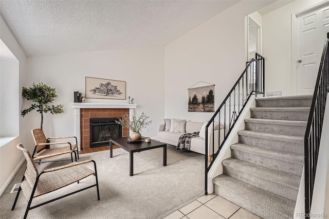 living room with a tiled fireplace, stairway, tile patterned floors, vaulted ceiling, and a textured ceiling