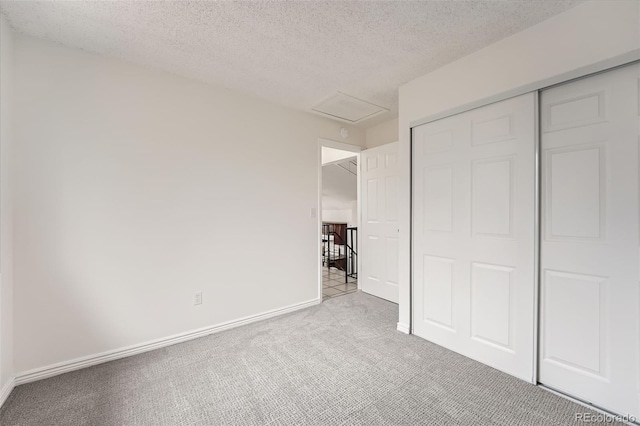 unfurnished bedroom featuring carpet, a closet, attic access, a textured ceiling, and baseboards