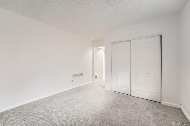 unfurnished bedroom featuring a textured ceiling, carpet floors, visible vents, baseboards, and a closet