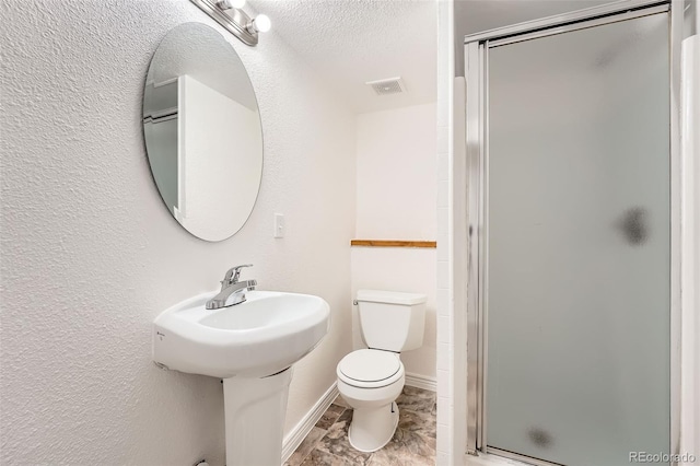 bathroom with a textured ceiling, a textured wall, a stall shower, and toilet