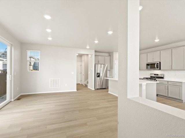 kitchen featuring gray cabinetry, backsplash, light hardwood / wood-style flooring, and appliances with stainless steel finishes