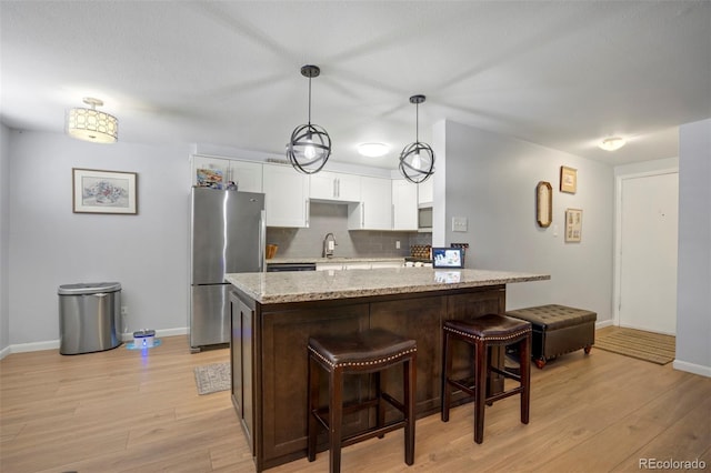 kitchen with decorative backsplash, baseboards, freestanding refrigerator, light wood finished floors, and white cabinetry