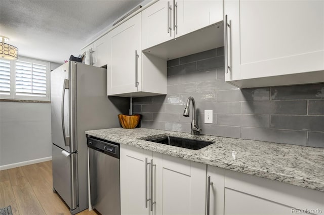 kitchen with dishwasher, a sink, baseboards, white cabinets, and light wood-style flooring
