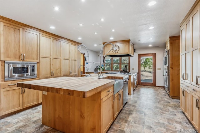 kitchen with a center island with sink, stainless steel appliances, light brown cabinets, and wood counters