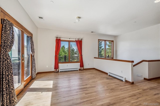 unfurnished room featuring a healthy amount of sunlight, light wood-type flooring, and a baseboard heating unit