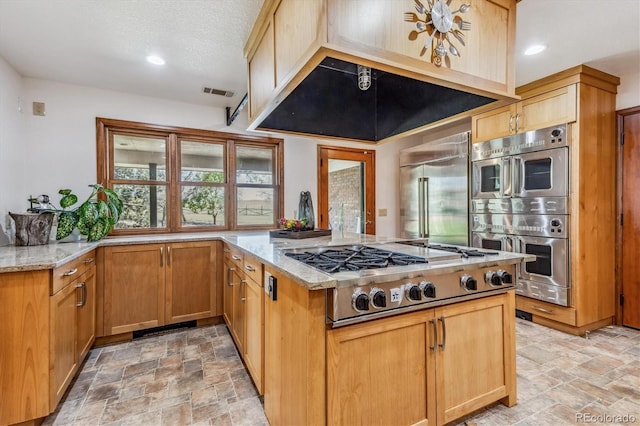 kitchen featuring kitchen peninsula, appliances with stainless steel finishes, a textured ceiling, and light stone counters