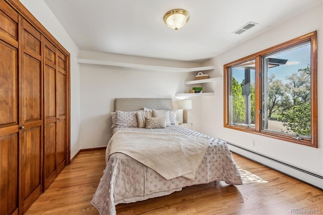 bedroom featuring a closet, a baseboard heating unit, and light wood-type flooring