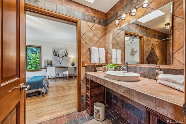 bathroom featuring wood-type flooring, a skylight, tile walls, and sink