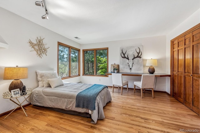 bedroom with light wood-type flooring, rail lighting, and a closet