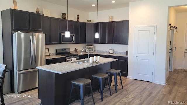 kitchen with appliances with stainless steel finishes, sink, an island with sink, light wood-type flooring, and a breakfast bar area