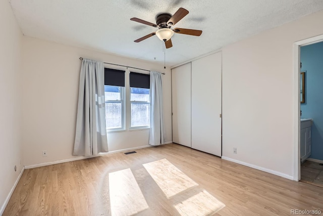 unfurnished bedroom with ceiling fan, ensuite bath, light wood-type flooring, a closet, and a textured ceiling