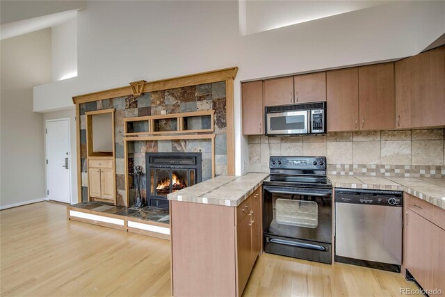 21650 US Highway 6 Unit 2096, Dillon, CO 80435 - kitchen featuring stainless steel appliances, light wood-style floors, a peninsula, a tiled fireplace, and backsplash