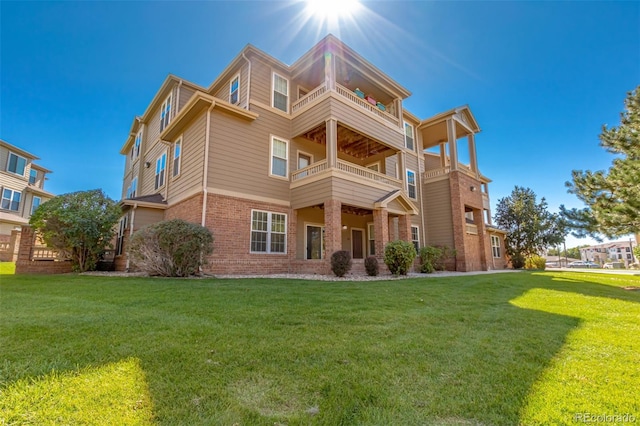 rear view of property with brick siding, a lawn, and a balcony