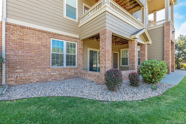 property entrance with a balcony, a lawn, and brick siding