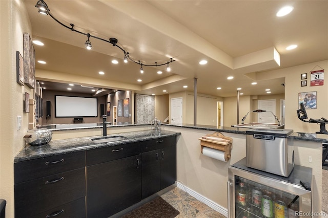 kitchen featuring a sink, dark cabinets, a tray ceiling, baseboards, and recessed lighting