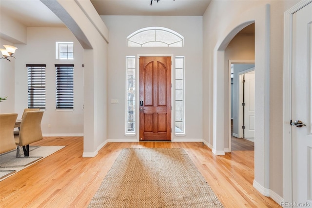 entrance foyer with light wood-style floors, arched walkways, and baseboards