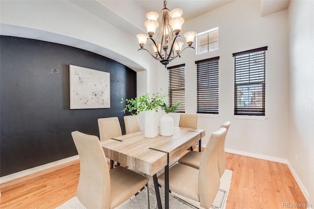 dining area featuring baseboards, an accent wall, a notable chandelier, and light wood-style floors