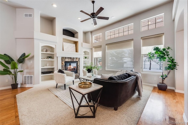 living room with built in shelves, wood finished floors, visible vents, and a premium fireplace