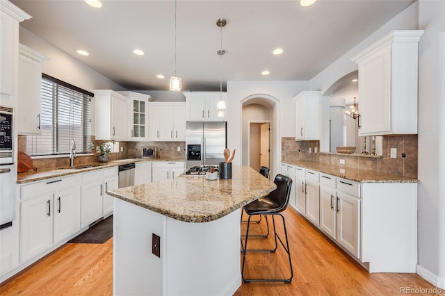 kitchen featuring arched walkways, decorative light fixtures, appliances with stainless steel finishes, white cabinetry, and a kitchen island