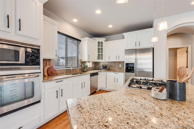 kitchen featuring light stone counters, decorative light fixtures, stainless steel appliances, glass insert cabinets, and white cabinets