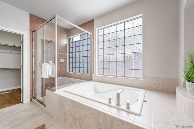 bathroom with a bath, a spacious closet, a stall shower, and a wealth of natural light