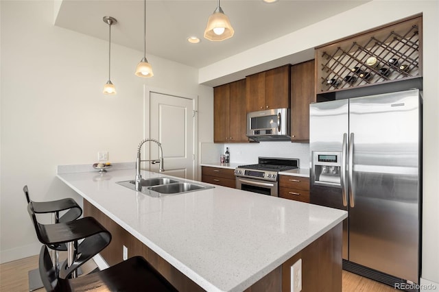 kitchen with kitchen peninsula, light wood-type flooring, stainless steel appliances, sink, and pendant lighting