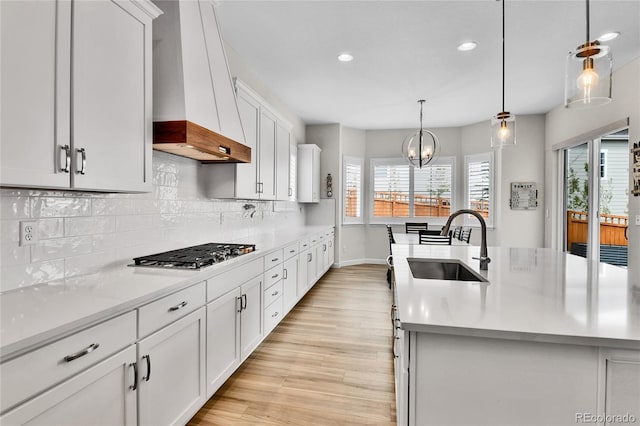 kitchen with recessed lighting, stainless steel gas stovetop, a sink, wall chimney exhaust hood, and light countertops