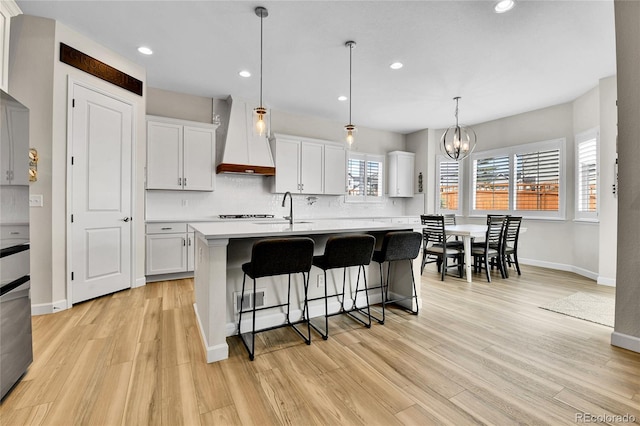 kitchen featuring light wood-style flooring, a breakfast bar area, baseboards, premium range hood, and light countertops