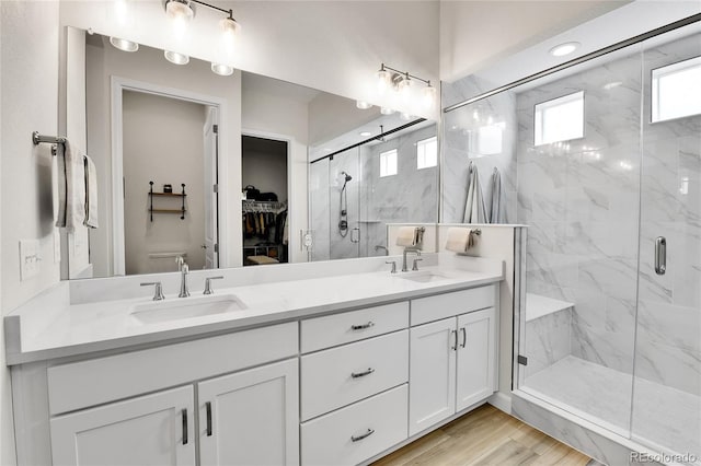 bathroom featuring double vanity, a marble finish shower, wood finished floors, and a sink
