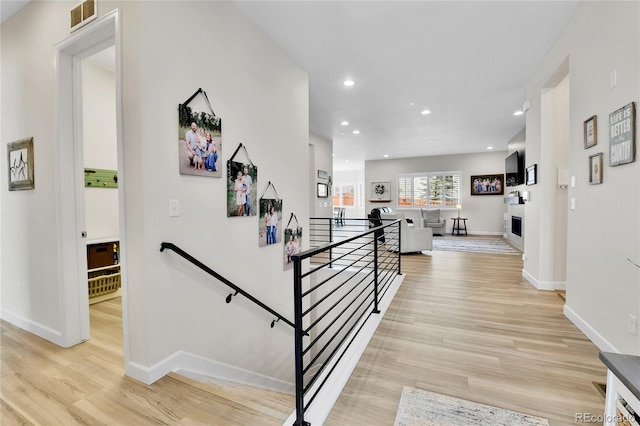 hall with an upstairs landing, recessed lighting, visible vents, baseboards, and light wood-style floors