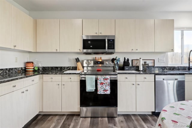 kitchen with cream cabinetry, appliances with stainless steel finishes, dark hardwood / wood-style floors, and dark stone countertops